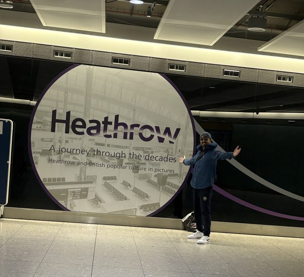 A person stands in front of a large Heathrow Airport sign that reads 'Heathrow: A journey through the decades' inside the terminal.